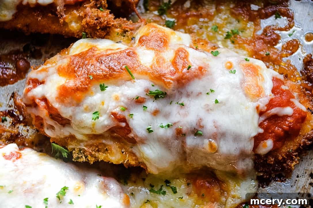 Golden brown crispy chicken parmesan with melted mozzarella and marinara sauce on a baking sheet.