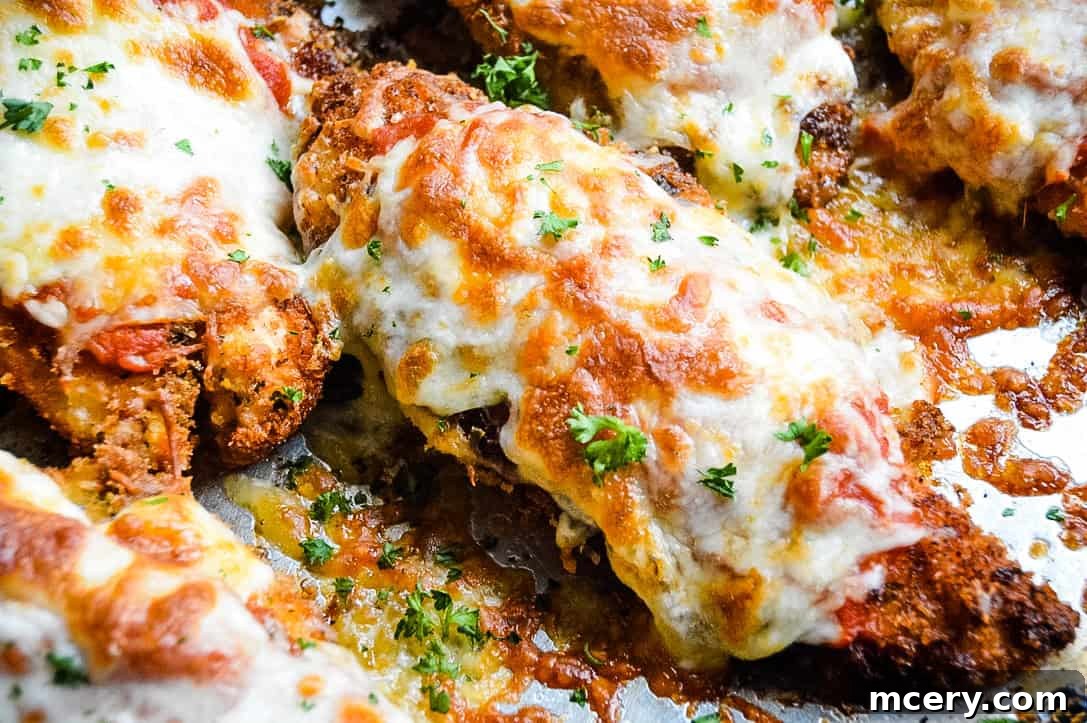 Crispy Chicken Parmesan served on a plate with pasta, garnished with fresh herbs.