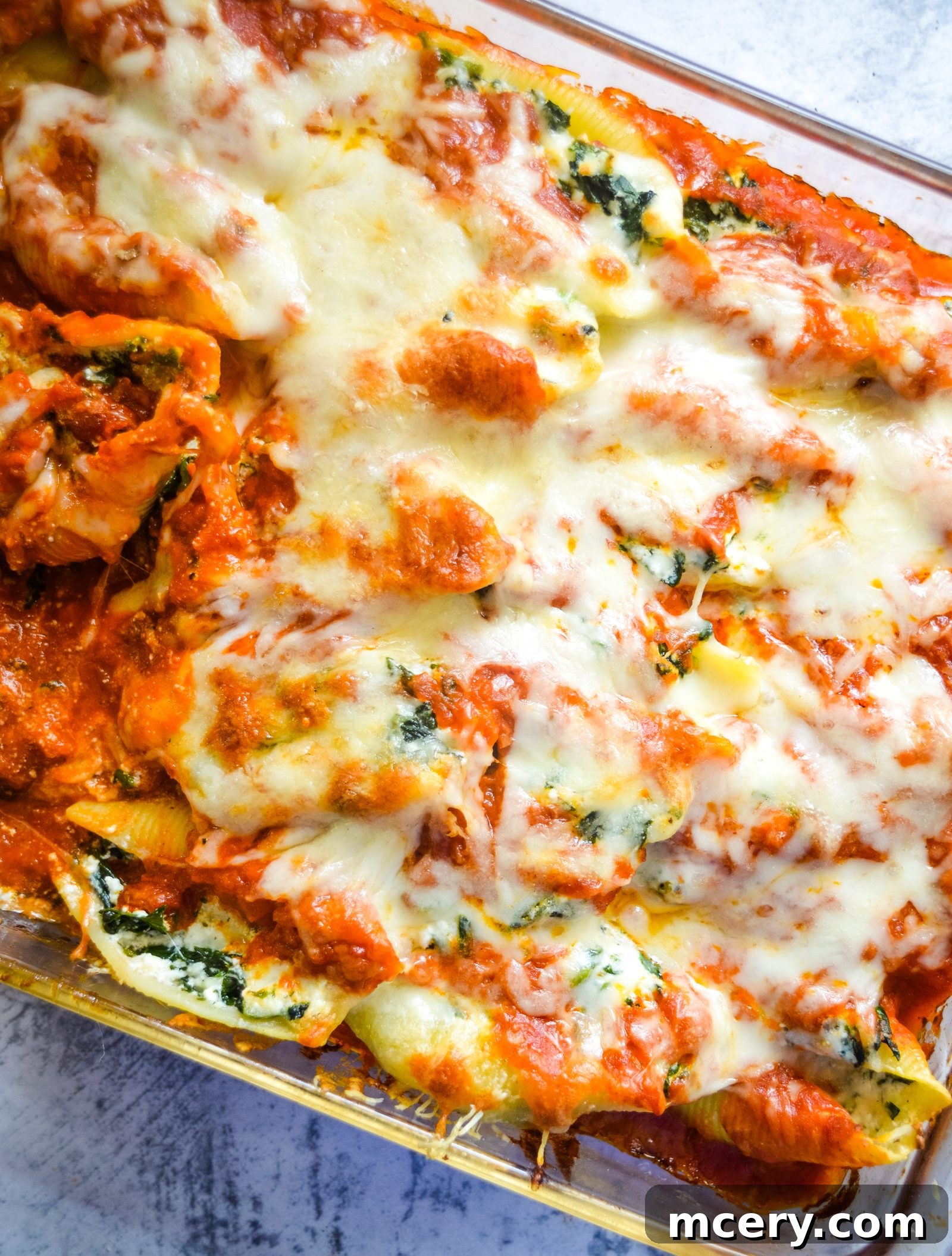 Spinach and Ricotta Stuffed Shells Bake 2 A vibrant close-up of baked spinach and cheese jumbo stuffed shells, topped with melted mozzarella and marinara sauce, garnished with fresh basil. The shells are perfectly golden and bubbling, resting on a rustic wooden surface.