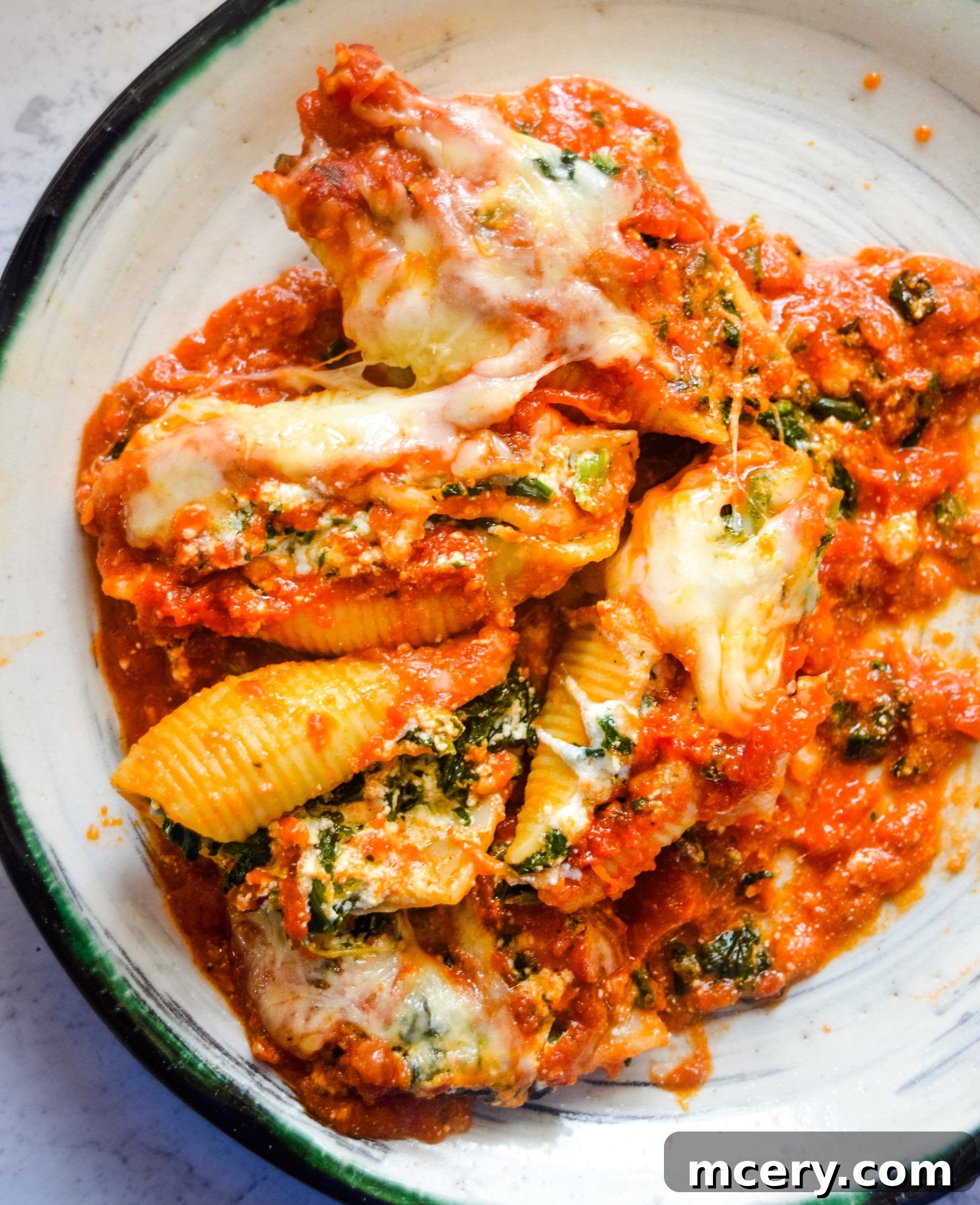 Spinach and Ricotta Stuffed Shells Bake 4 A close-up shot of a single jumbo pasta shell, perfectly stuffed with a creamy spinach and cheese mixture, held delicately with tongs and ready to be placed into a baking dish.