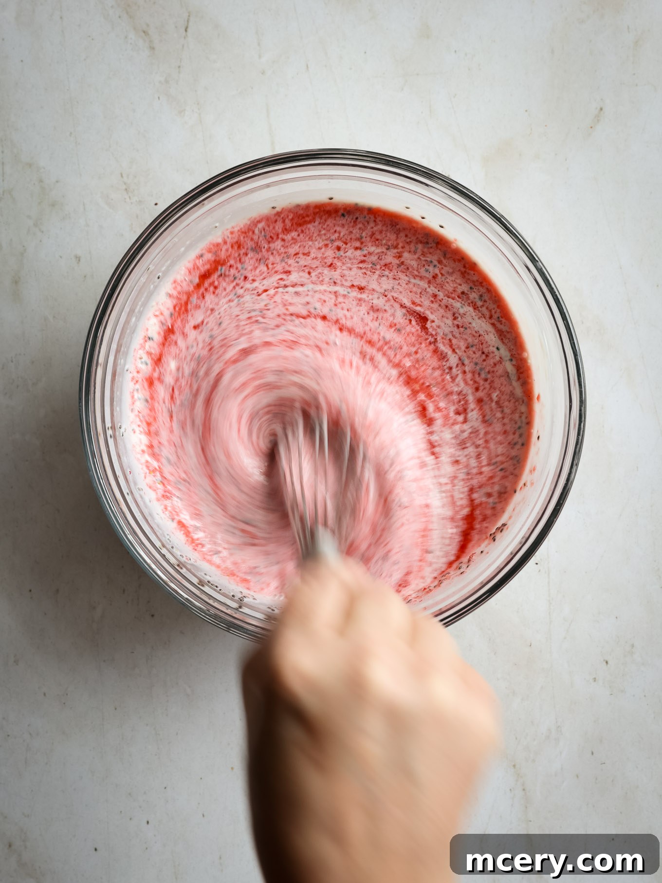 Delightful Strawberry Chia Pudding 6 Pureed strawberries being whisked into the yogurt and chia seed mixture in a glass bowl.