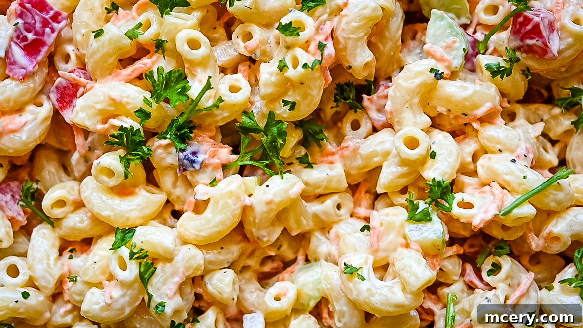 A vibrant, creamy macaroni salad in a large serving bowl, mixed with finely chopped red bell pepper, celery, and red onion, garnished with fresh parsley.