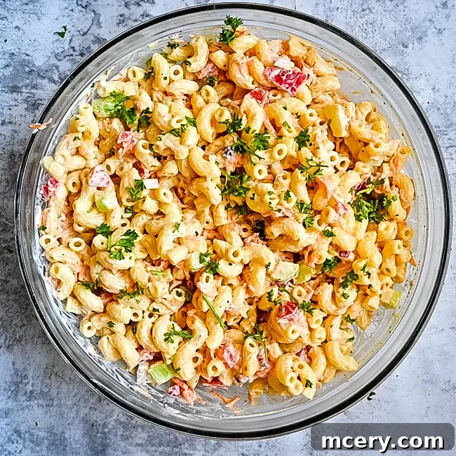 A refreshing serving of macaroni salad in a clear glass bowl, showcasing its layered colors and creamy consistency.