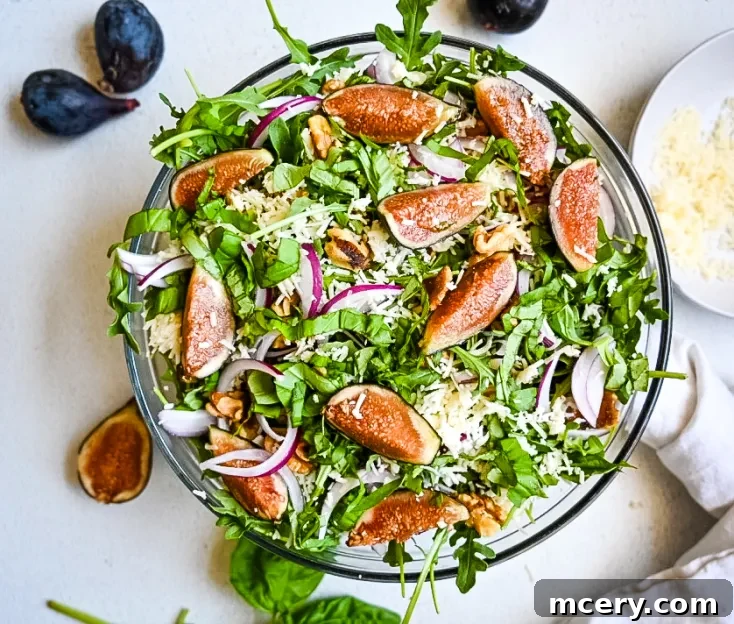A vibrant Fresh Fig and Arugula Salad featuring fresh arugula leaves, sliced figs, red onion slivers, grated cheese, and walnut pieces, all tossed together in a glass bowl. The ingredients are colorful and arranged in an appetizing manner.