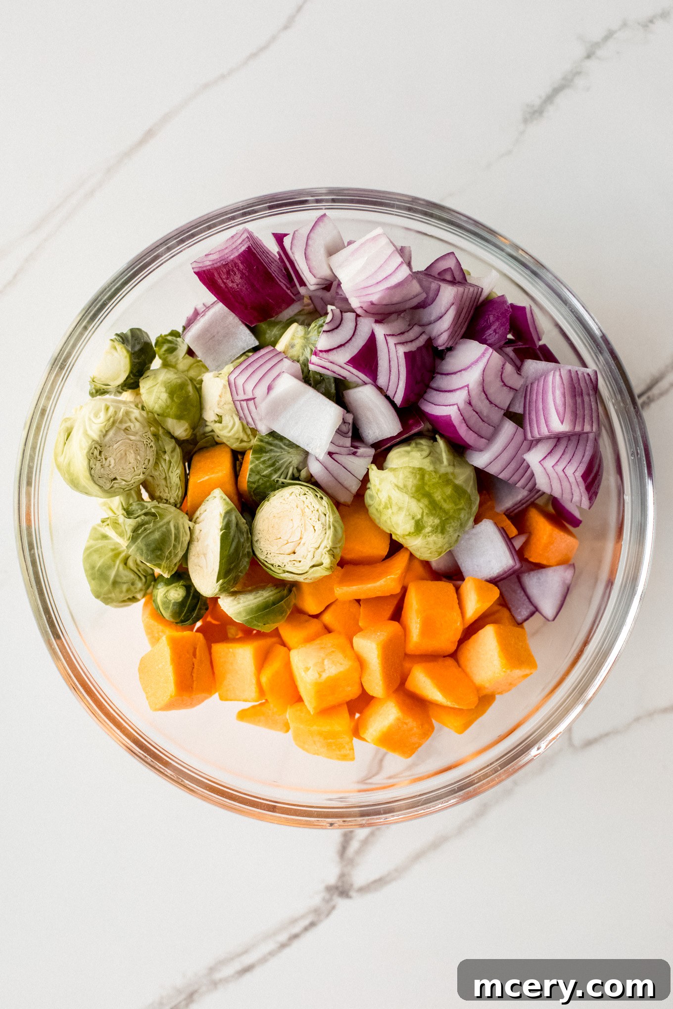 Autumn Roasted Bounty 4 Cut butternut squash, Brussels sprouts, and red onion in a large glass bowl, ready for seasoning.