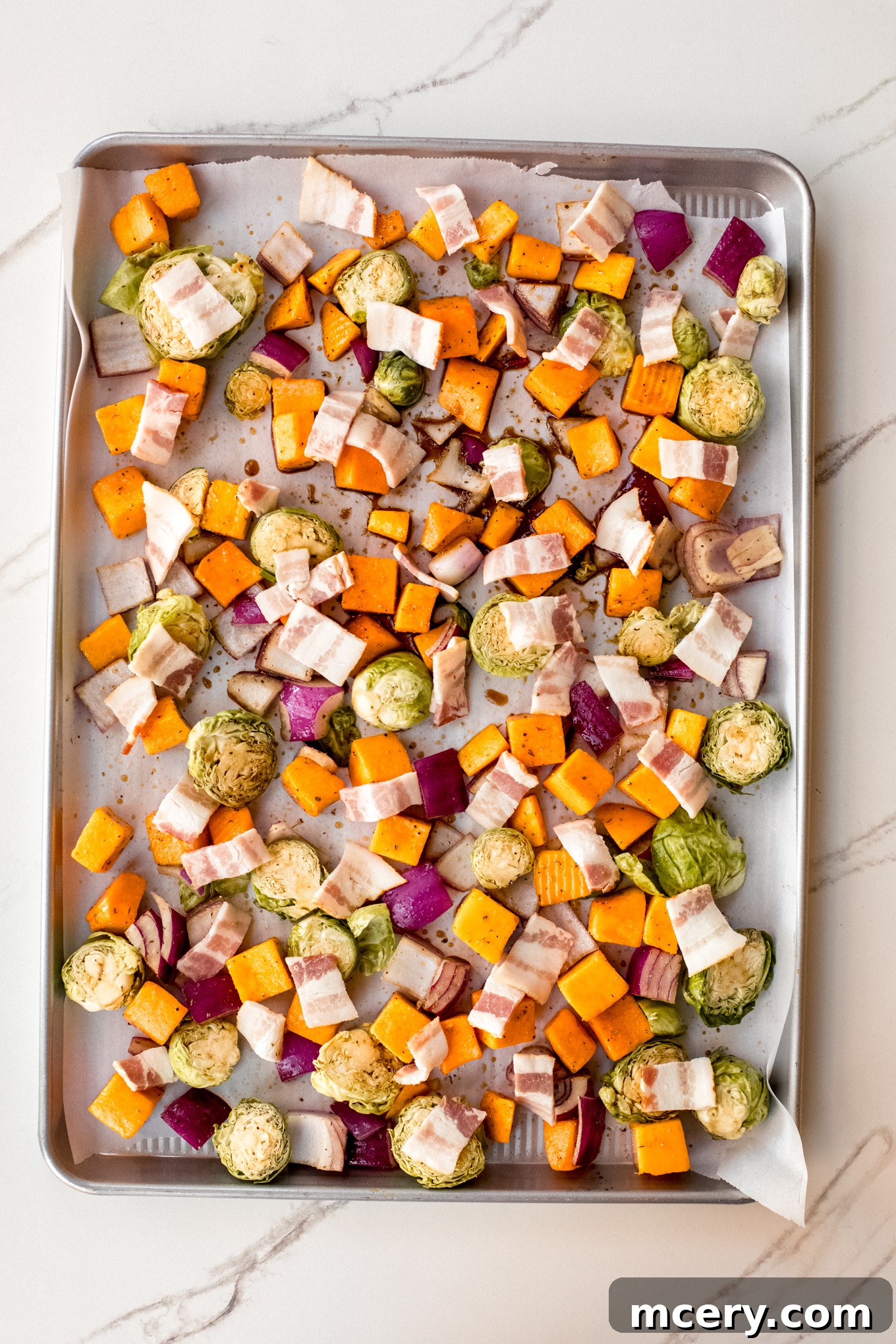 Autumn Roasted Bounty 7 Raw, seasoned vegetables and bacon bits spread out on a parchment-lined baking sheet.