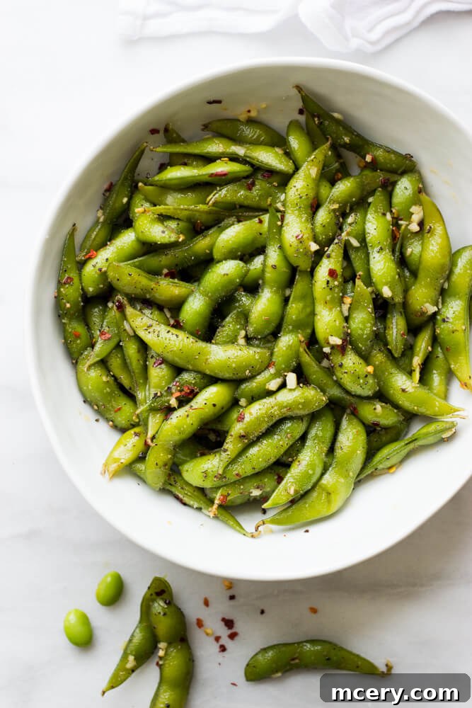 Fiery Garlic Edamame 5 Cooked edamame being tossed in a skillet with melted garlic butter and chili flakes.