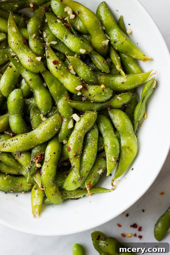 Fiery Garlic Edamame 6 A bowl of spicy garlic edamame, perfectly seasoned and ready to eat, with a hand reaching for a pod.