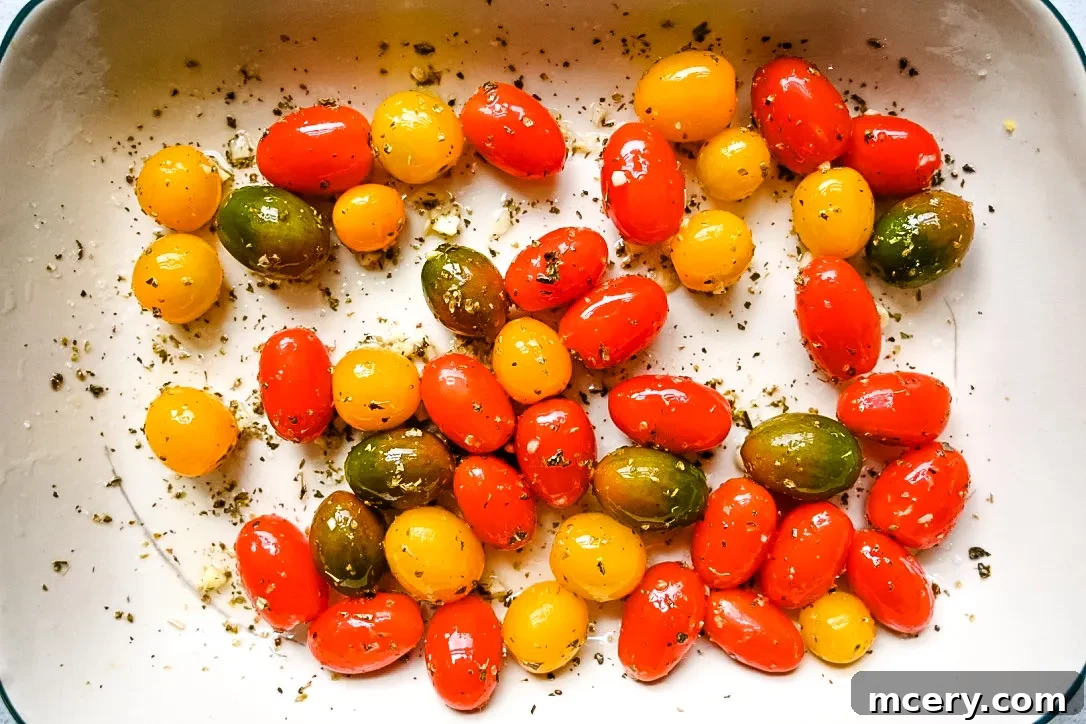 Fresh cherry tomatoes tossed with olive oil, herbs, and garlic in a baking dish, ready for roasting.