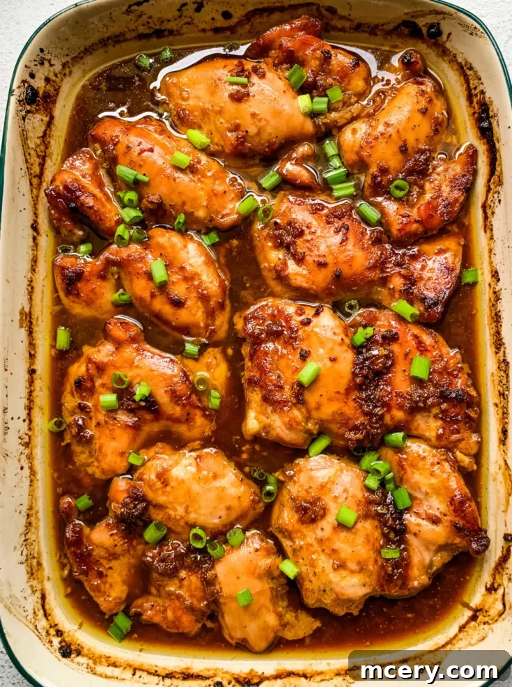A close-up view of cooked, glazed Garlic Brown Sugar Chicken pieces garnished with chopped green onions. The chicken is browned and covered in a savory sauce, giving it a succulent and flavorful appearance. The dish is presented in a baking dish.