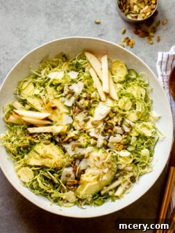 shredded Brussels sprouts salad in a white bowl with wooden utensils on the side.