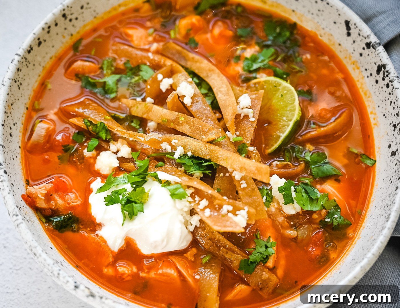Speedy Southwestern Chicken Tortilla Soup 2 A vibrant bowl of chicken tortilla soup, garnished with zesty lime tortilla strips, fresh cilantro, a dollop of sour cream, and a lime wedge. The rich broth is visible, along with chunks of chicken and vegetables.