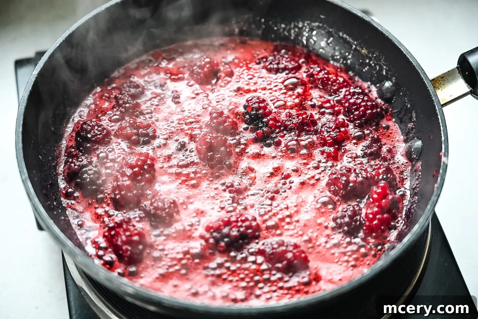 A small saucepan with fresh blackberries, lemon zest, lemon juice, and honey simmering to create the compote. The berries are partially mashed, and steam rises from the pan.