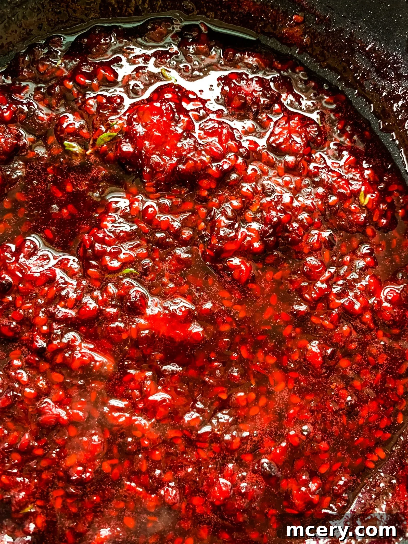 A close-up of fresh thyme being added to the simmering blackberry compote, infusing it with aromatic flavor.