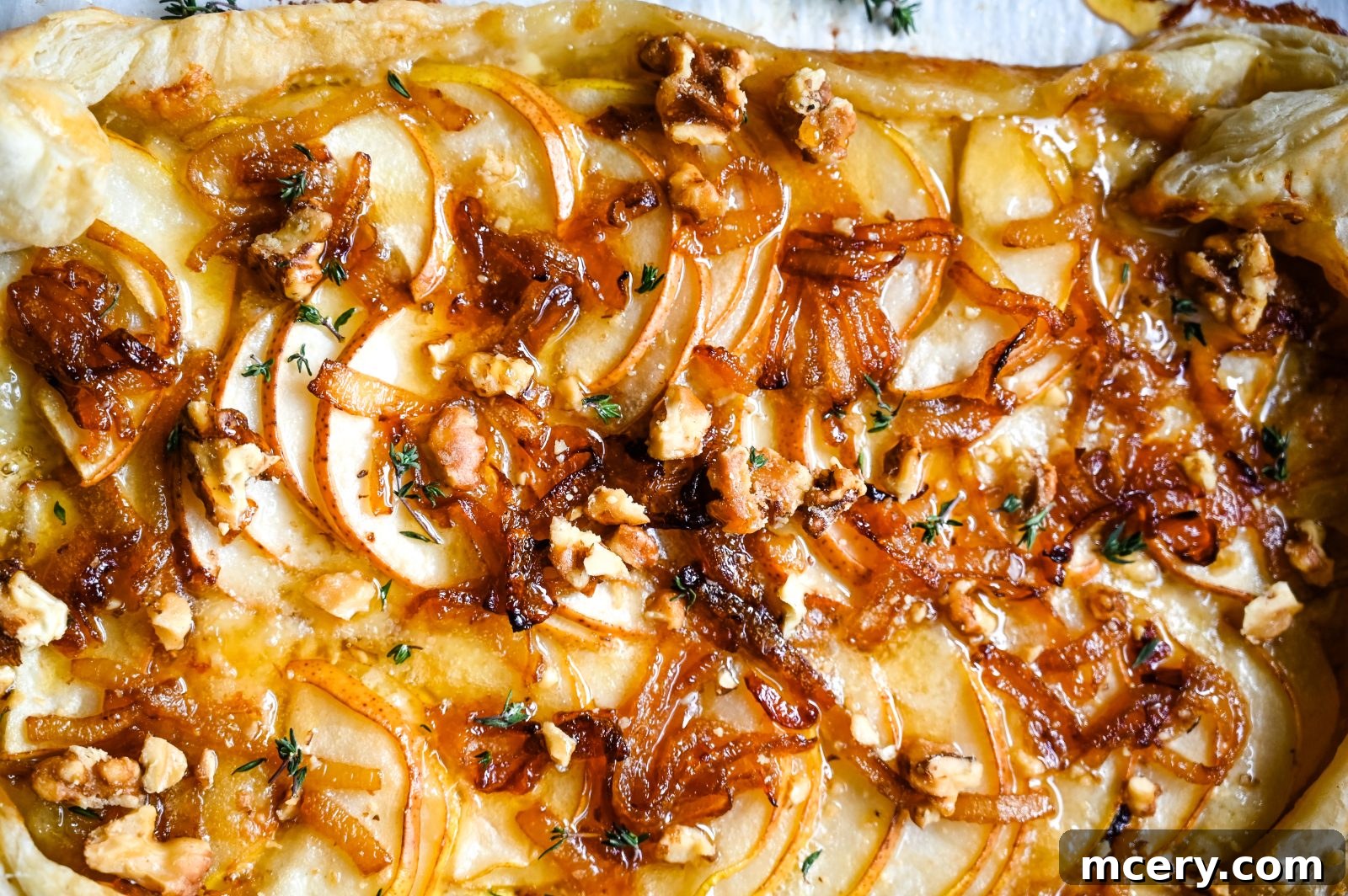 A beautifully golden Brie and Pear Puff Pastry Tart, garnished with fresh thyme and candied pecans, featuring melted Brie and sliced pears on a flaky crust.