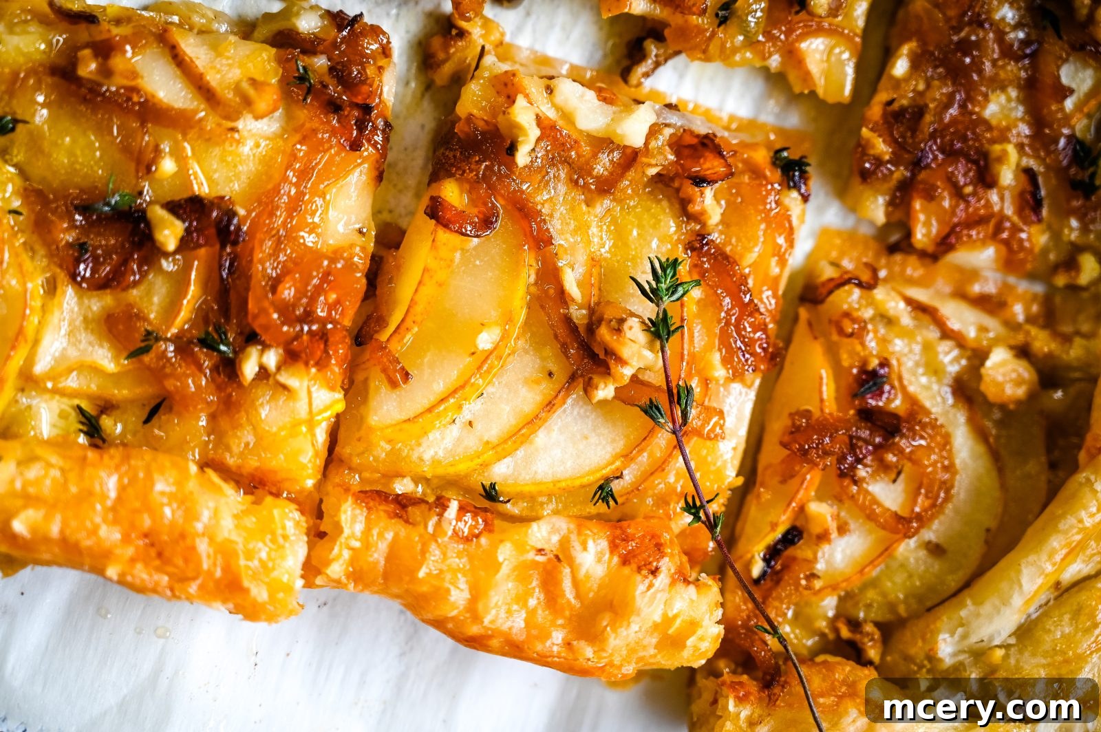 Individual ingredients for the Brie and Pear Puff Pastry Tart artfully arranged: a round of Brie, sliced pears, fresh thyme sprigs, candied pecans, and golden caramelized onions.
