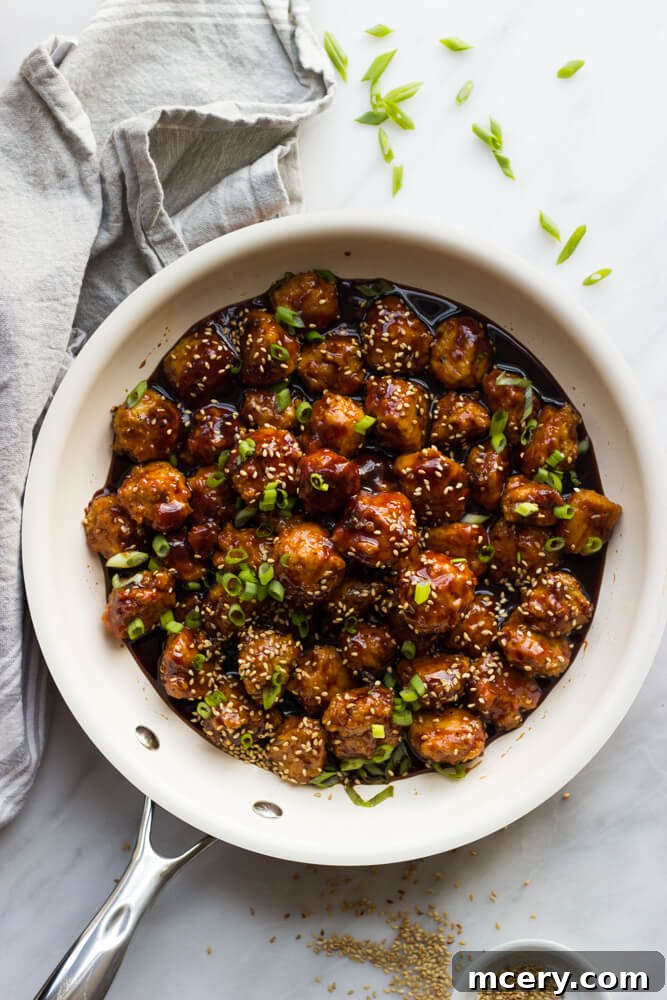 Sticky Asian Chicken Meatballs 2 asian chicken meatballs in a skillet garnished with green onions.