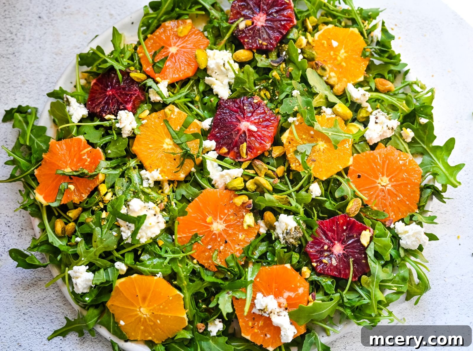 Effortless Citrus Delight 5 The finished Easy Citrus Salad beautifully plated, showcasing the layered ingredients of arugula, various citrus slices, crumbled goat cheese, and pistachios, drizzled with vinaigrette. Ready to be served.