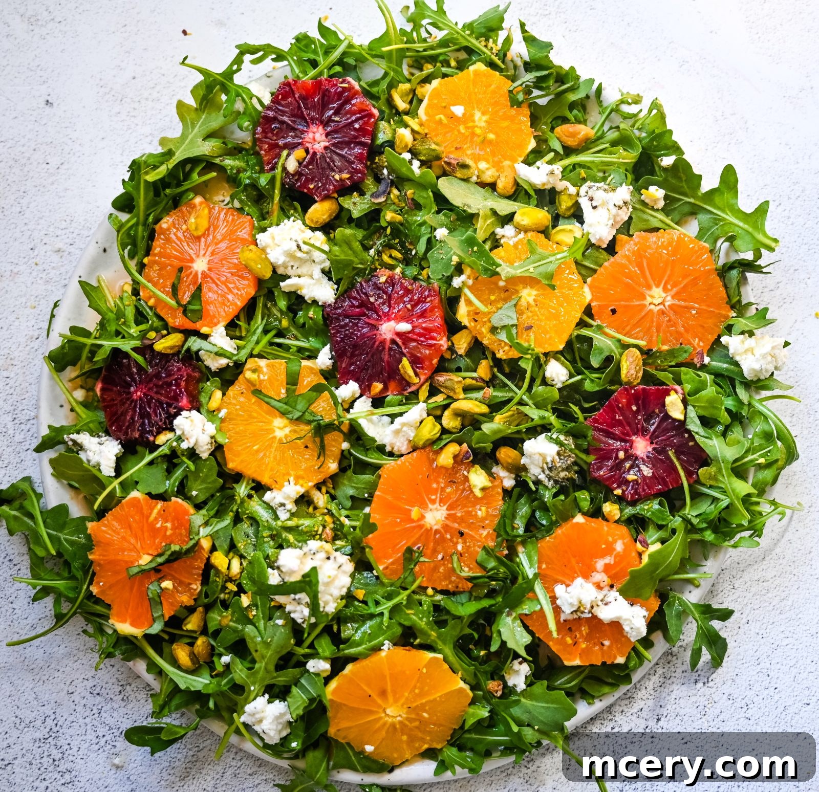 A vibrant Easy Citrus Salad with mixed greens, blood orange and mandarin slices, crumbled feta cheese, and scattered pistachios, displayed on a white plate.