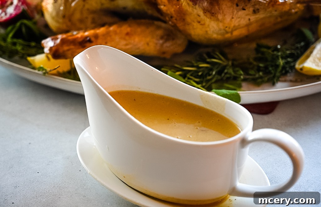 Skip the Brine! Your Easiest, Juiciest Thanksgiving Turkey Ever 12 A white gravy boat filled with creamy, golden-brown turkey gravy sits on a matching white saucer. Some green herbs are partially visible in the background, slightly out of focus, on a white surface.