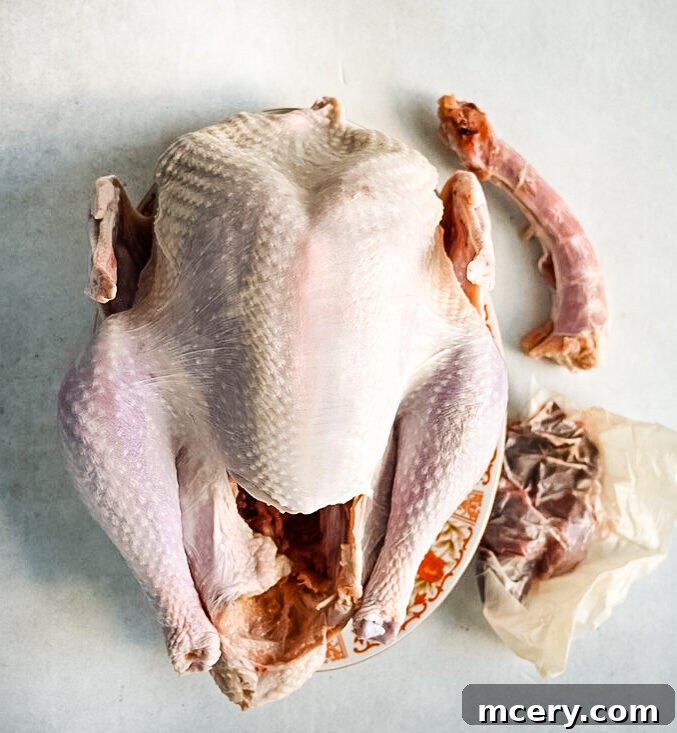 Skip the Brine! Your Easiest, Juiciest Thanksgiving Turkey Ever 8 A raw, whole turkey placed on a plate with its neck and giblets beside it on a light-colored surface. The turkey is prepped and ready for further preparation or cooking.