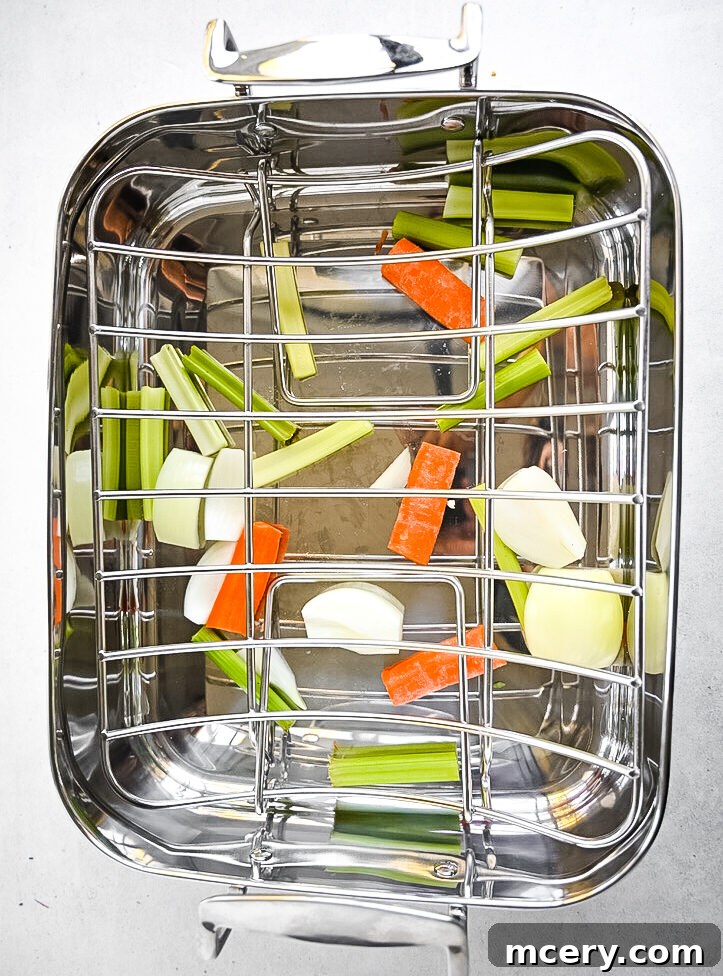 Skip the Brine! Your Easiest, Juiciest Thanksgiving Turkey Ever 10 A stainless steel roasting pan with a metal rack inside holds chopped celery, carrots, and onion pieces scattered at the bottom. The vegetables appear fresh, and the pan is ready for roasting.