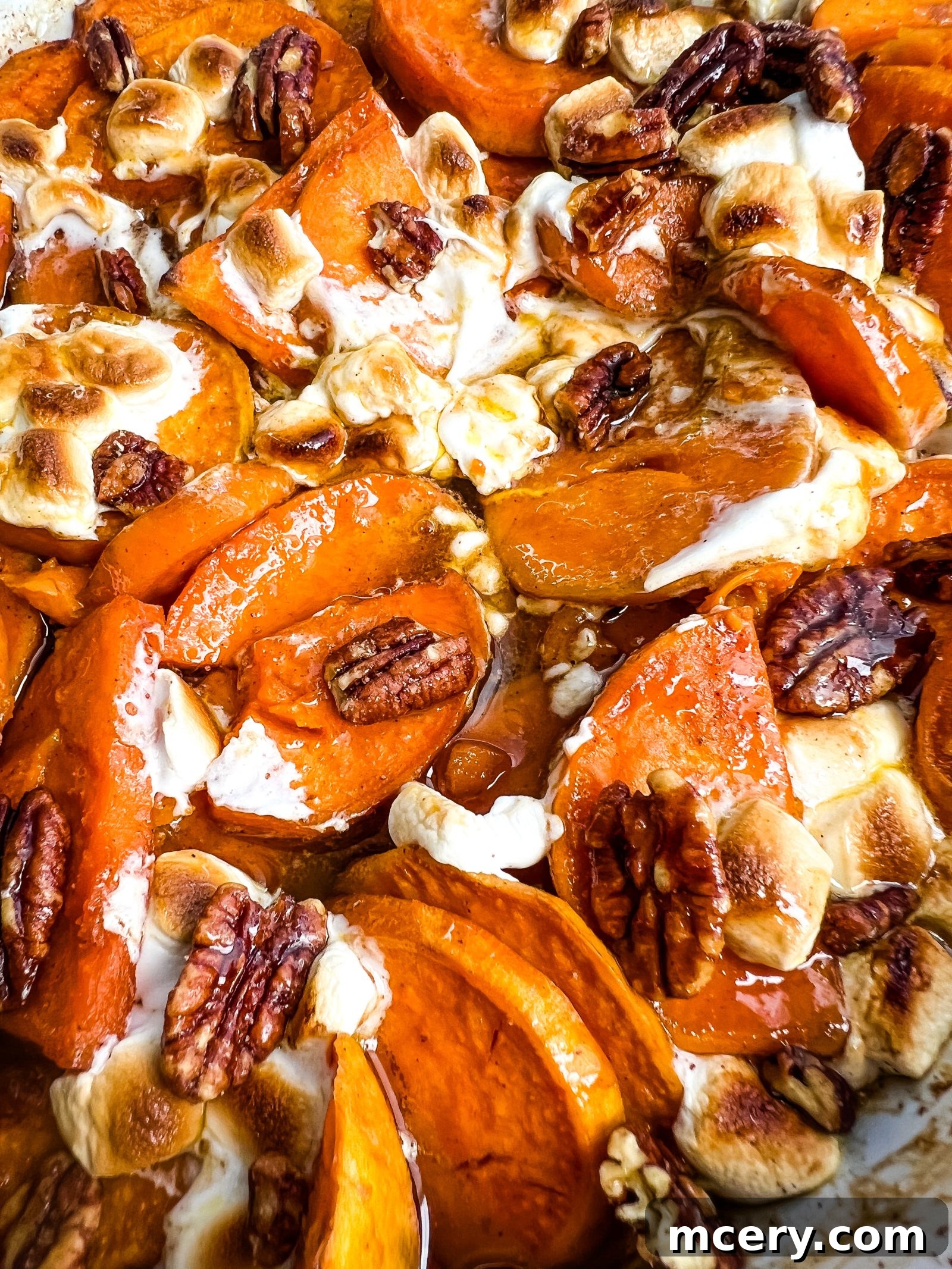 Decadent Candied Sweet Potatoes 7 A close-up of vibrant Candied Sweet Potatoes topped with toasted marshmallows, pecans, and a glaze. The sweet potatoes are sliced into rounds and layered with the other ingredients, creating a visually appealing and festive dish.