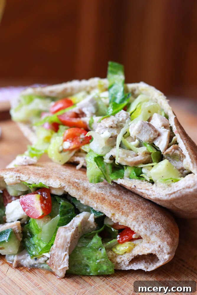 A close-up view of Greek chicken and romaine salad generously stuffed inside a whole wheat pita, showcasing the enticing layers of fresh ingredients.