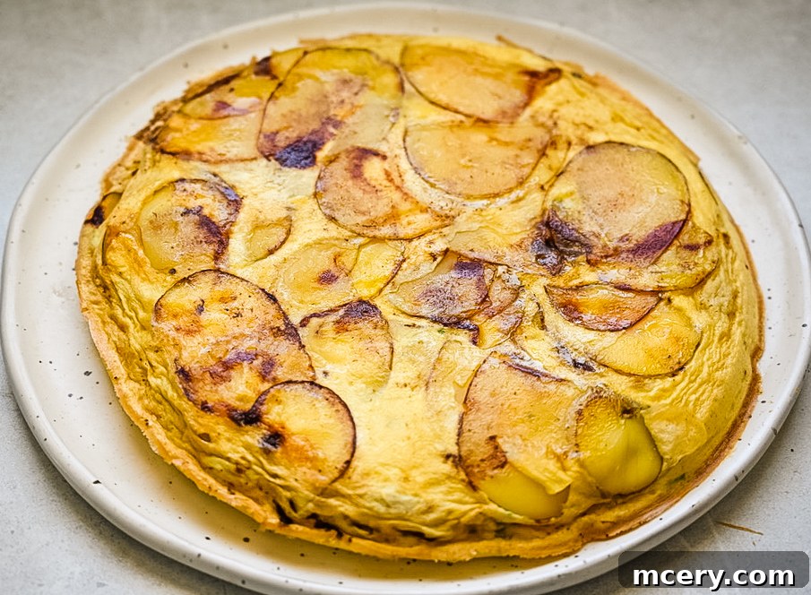 Effortless Egg Potato Frittata 10 A slice of egg and potato frittata topped with fresh tomato and chive mixture, on a white plate with a fork.