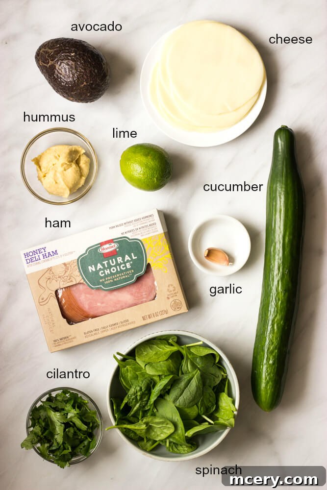 Refreshing Cucumber Bites 4 Ingredients laid out on a wooden board: cucumbers, ham, cheese, spinach, cilantro, avocado, and hummus