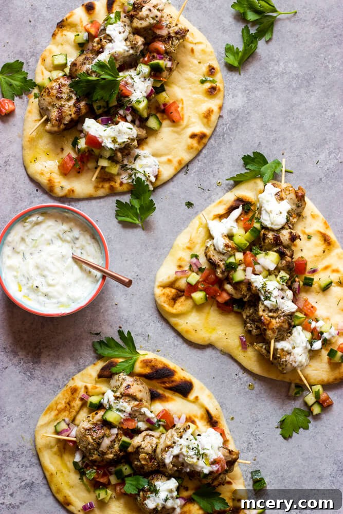 Homemade Chicken Gyro Perfection 2 Overhead shot of chicken gyro meat in warm naan bread, served with a fresh cucumber tomato salad and creamy tzatziki sauce.