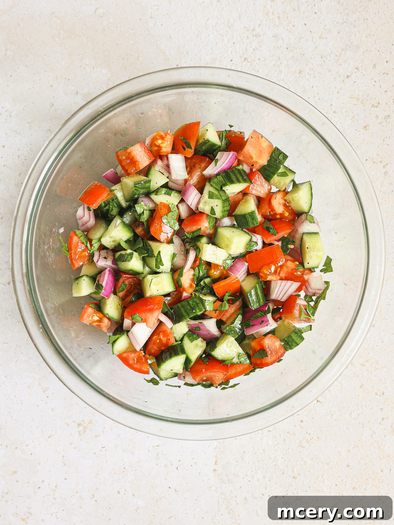 Homemade Chicken Gyro Perfection 7 Tossing cucumber tomato salad with dressing in a glass bowl.