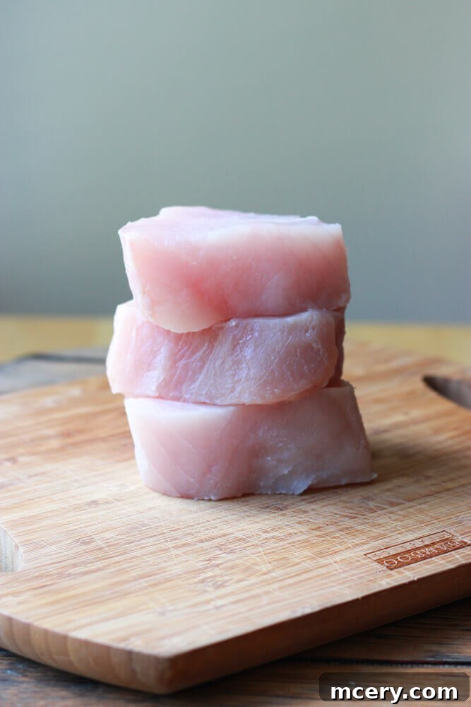 Fresh albacore tuna steaks, ready for preparation, stacked on a wooden cutting board.