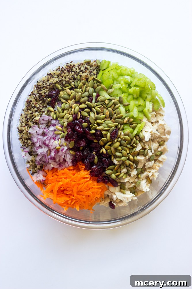 Mediterranean Chicken Quinoa Medley 5 cooked quinoa, shredded chicken, chopped vegetables, and dried cranberries in a large glass mixing bowl.