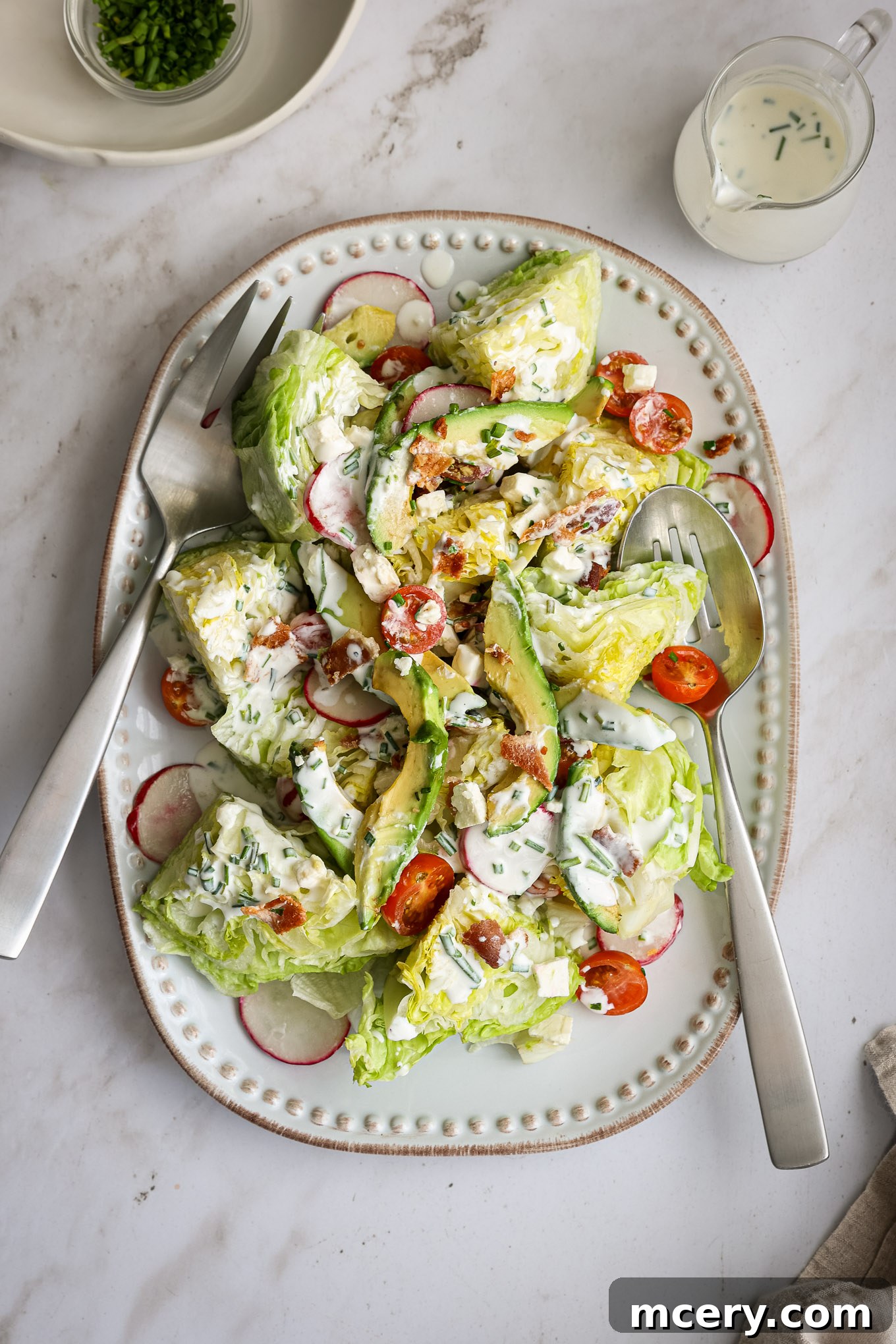 The Ultimate Chopped Wedge Salad 2 A beautifully presented chopped wedge salad on a white platter, generously garnished with vibrant avocado slices, thinly cut radishes, and cherry tomatoes, embodying freshness and appeal.