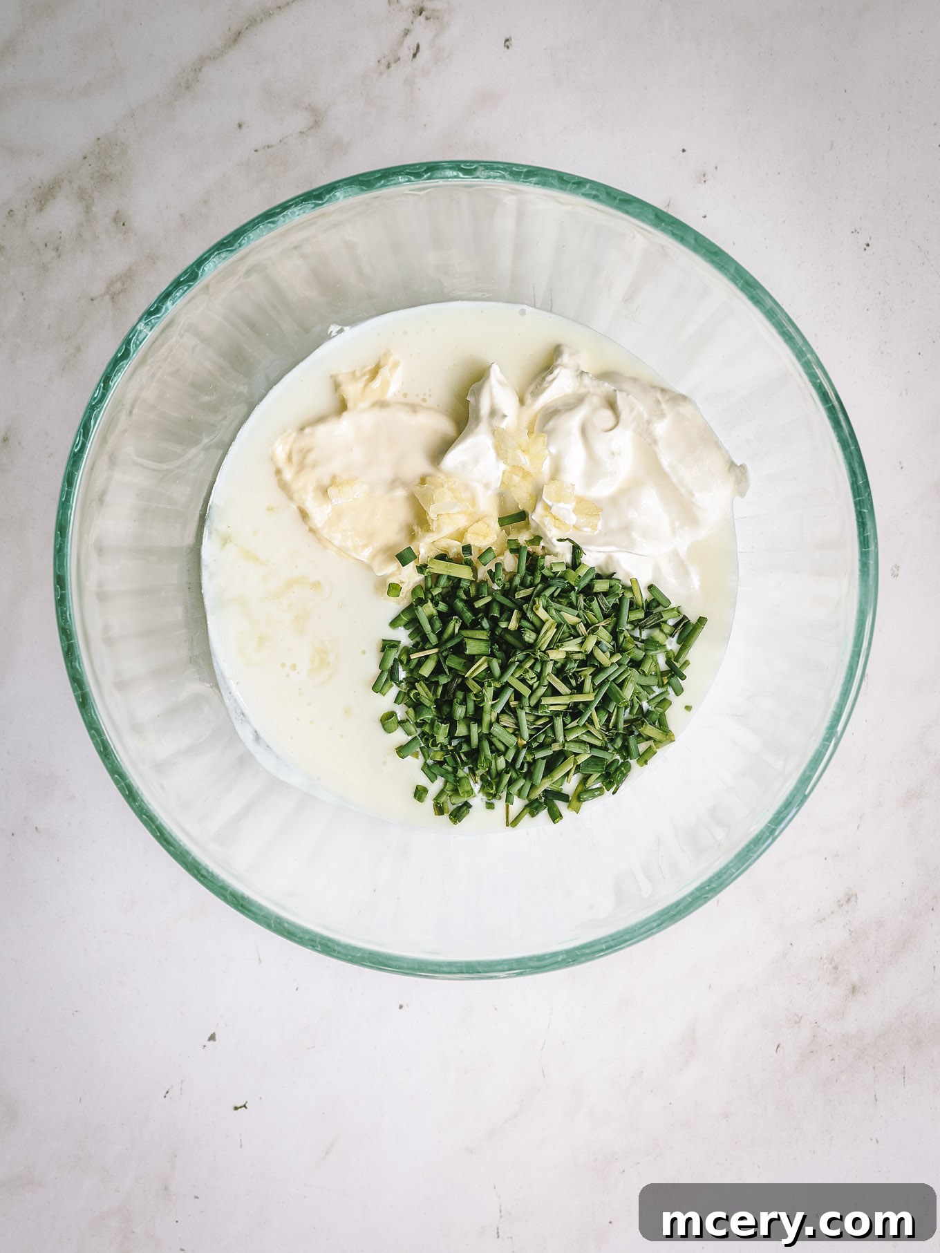 The Ultimate Chopped Wedge Salad 4 A glass bowl containing a vibrant mix of buttermilk, creamy mayonnaise, tangy sour cream, and fresh green chives, perfectly prepped for whisking into a delicious dressing.
