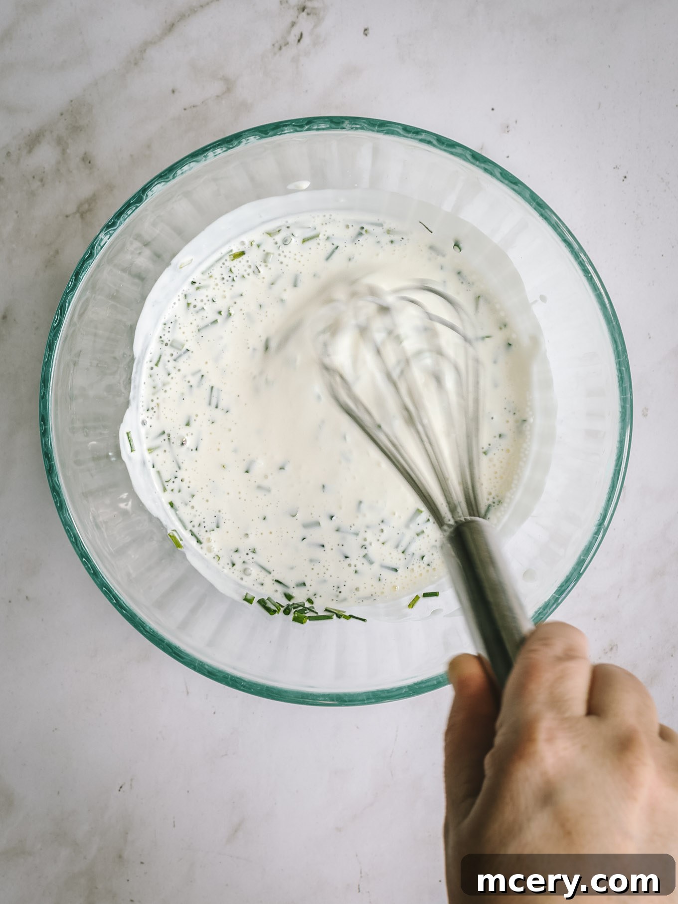 The Ultimate Chopped Wedge Salad 5 A whisked buttermilk dressing in a clear glass bowl, showcasing its smooth, creamy texture and readiness to perfectly coat the chopped wedge salad ingredients.