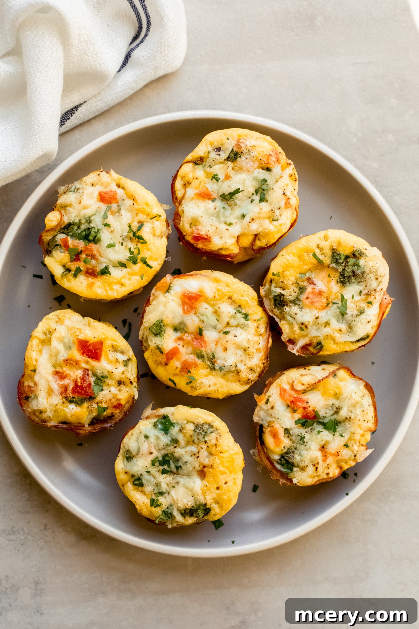 Savory Ham and Egg Breakfast Bites 2 Freshly baked ham and egg muffin cups beautifully arranged on a white plate, garnished with fresh herbs, ready for a delicious breakfast.