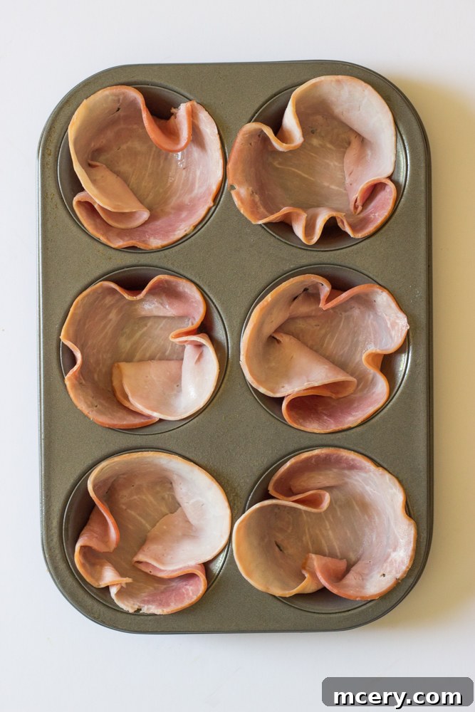 Savory Ham and Egg Breakfast Bites 4 A close-up view of a muffin tin, with each cup neatly lined with thin slices of deli ham, forming a perfect base for the egg muffins.