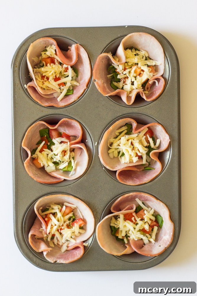 Savory Ham and Egg Breakfast Bites 5 A top-down view of a muffin tin with ham-lined cups, now filled with a colorful mixture of chopped spinach, onions, tomatoes, and shredded cheese, awaiting the egg mixture.