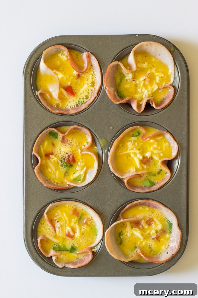 Savory Ham and Egg Breakfast Bites 7 A muffin tin, with ham-lined cups filled with a vibrant mix of vegetables and cheese, now topped with the whisked egg mixture, ready to be baked in the oven.
