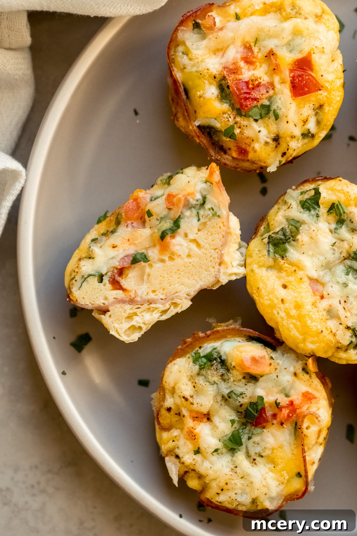 Savory Ham and Egg Breakfast Bites 8 A ham and egg muffin cup, cut in half to reveal its fluffy interior with layers of egg, spinach, tomatoes, and ham, presented beautifully on a plate.
