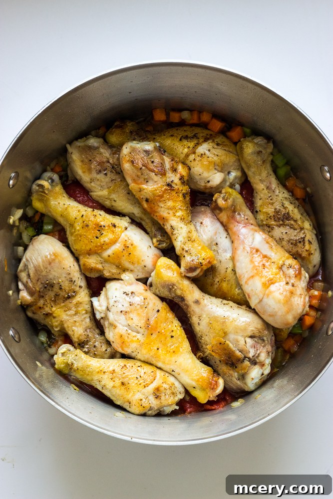 Simple Weeknight Chicken Cacciatore 7 seared chicken drumsticks layered over cooked vegetables inside dutch oven.